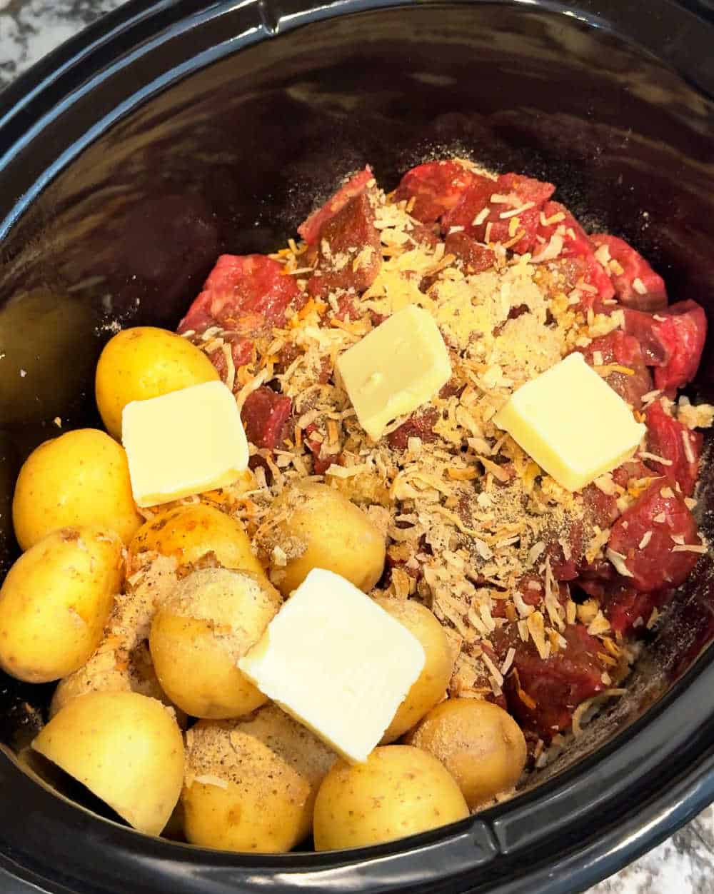 pats of butter on meat and potatoes in slow cooker.