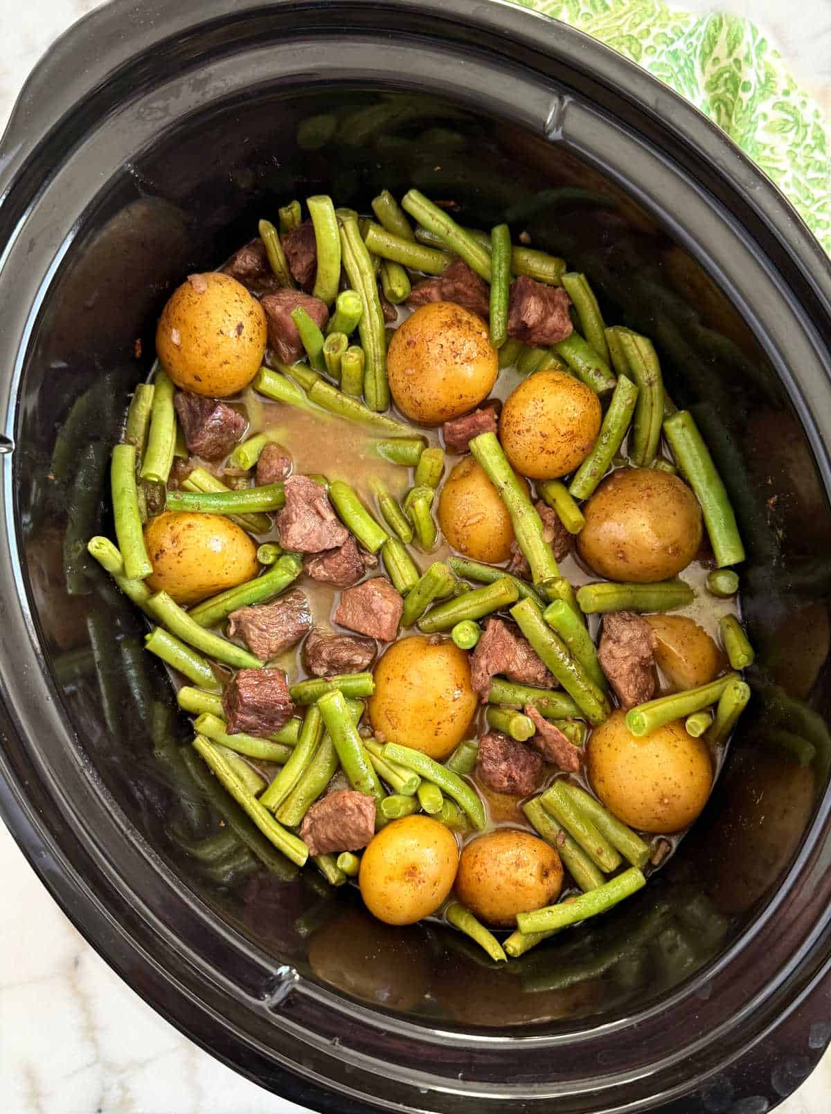 garlic butter beef bites and potatoes with green beans in slow cooker.