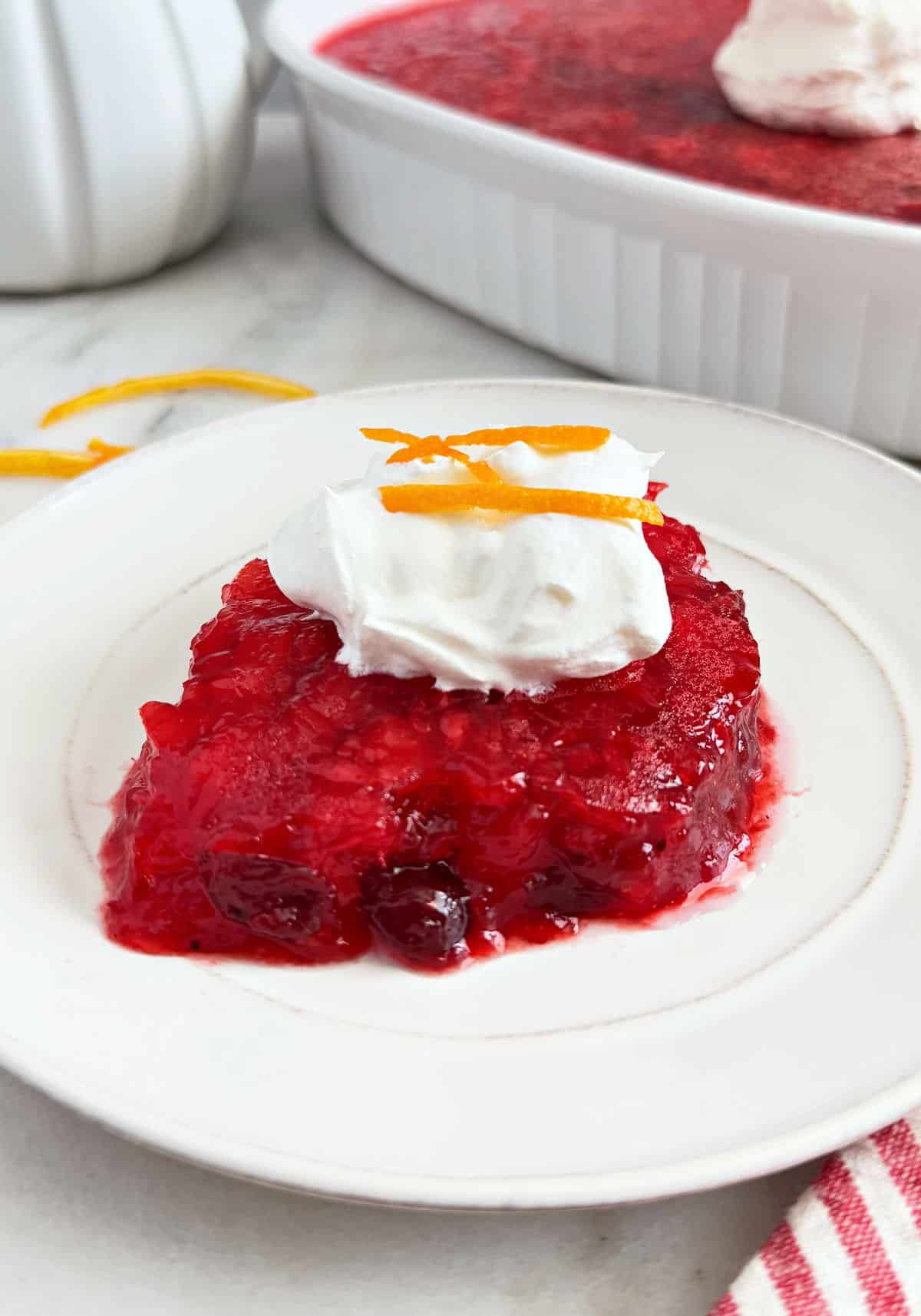 cranberry jello salad topped with cool whip and orange zest on plate.