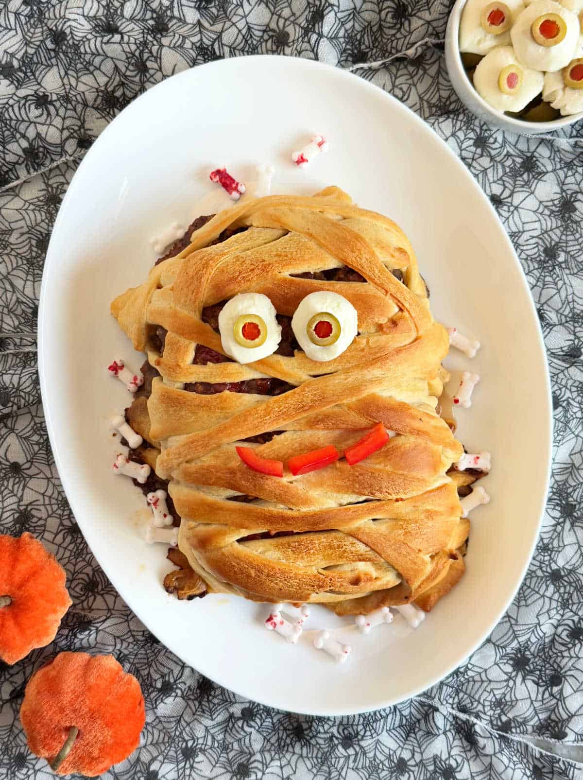 Halloween mummy meatloaf wrapped in crescent dough with olive eyes and pepper mouth.