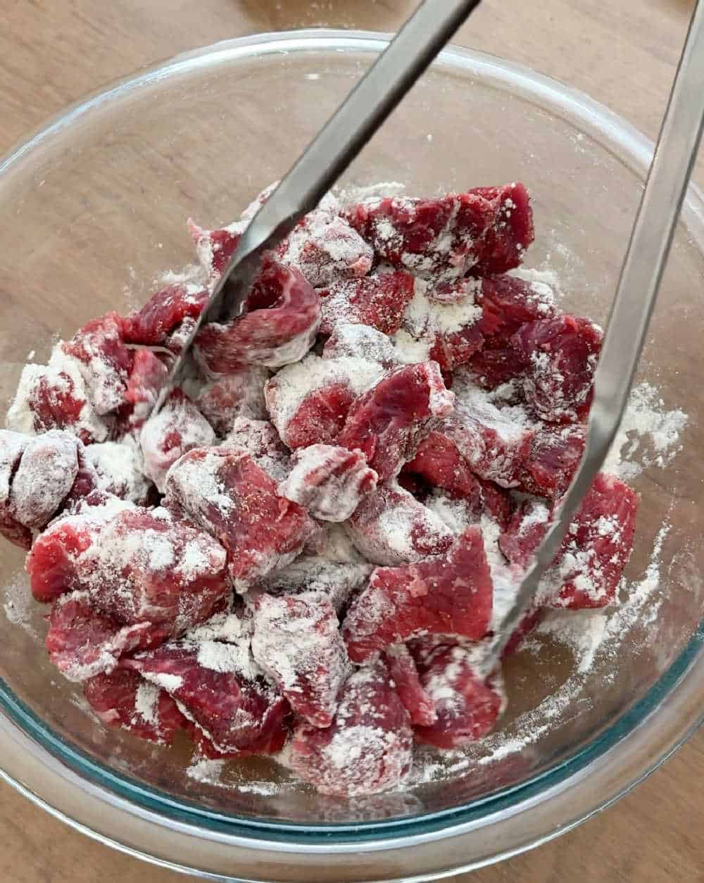 tossing beef cubes with flour in bowl.