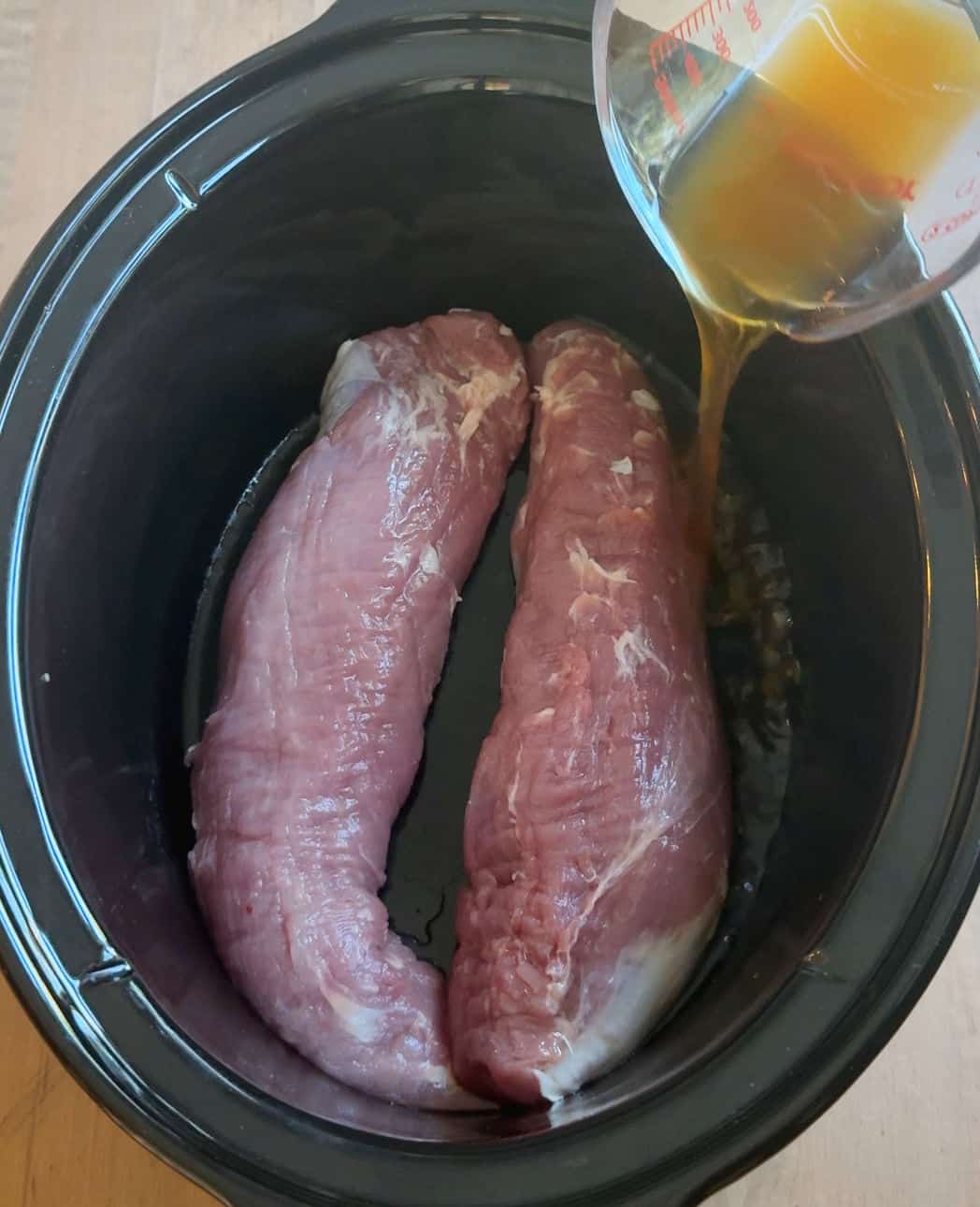pouring broth over tenderloin in slow cooker.