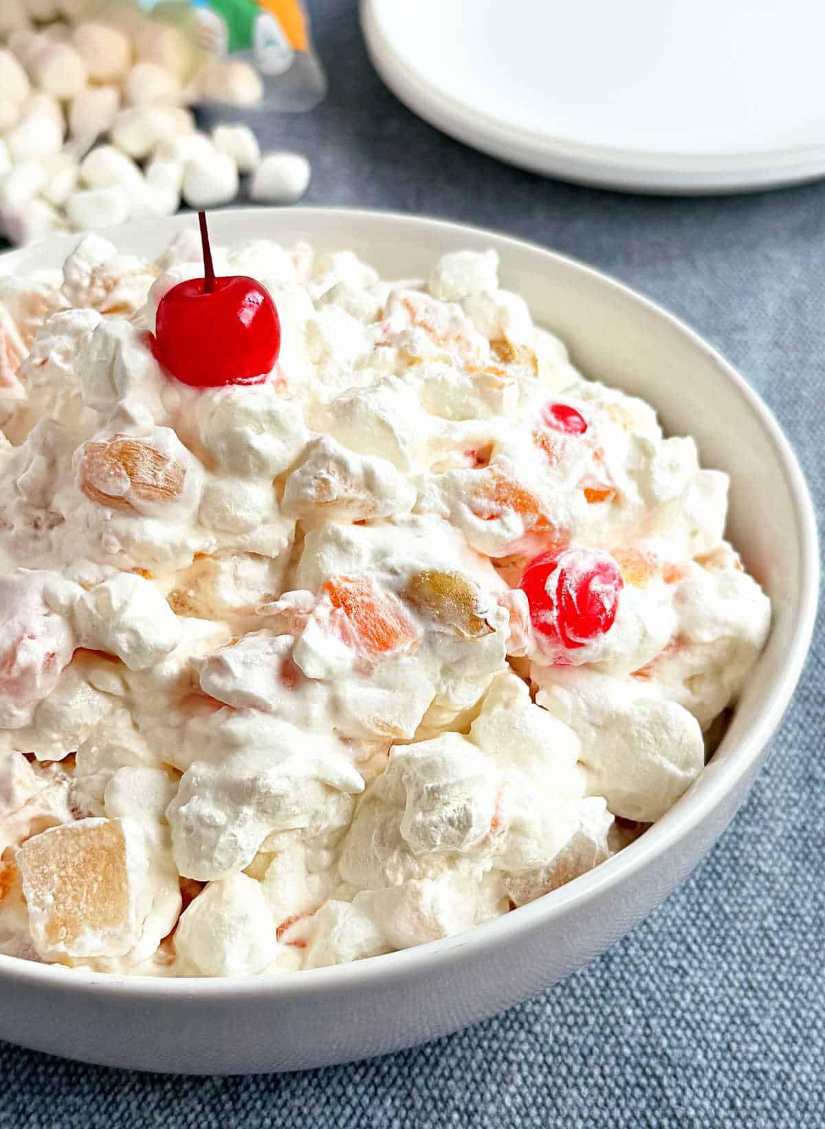 bowl of marshmallow fruit salad with cherry on top.