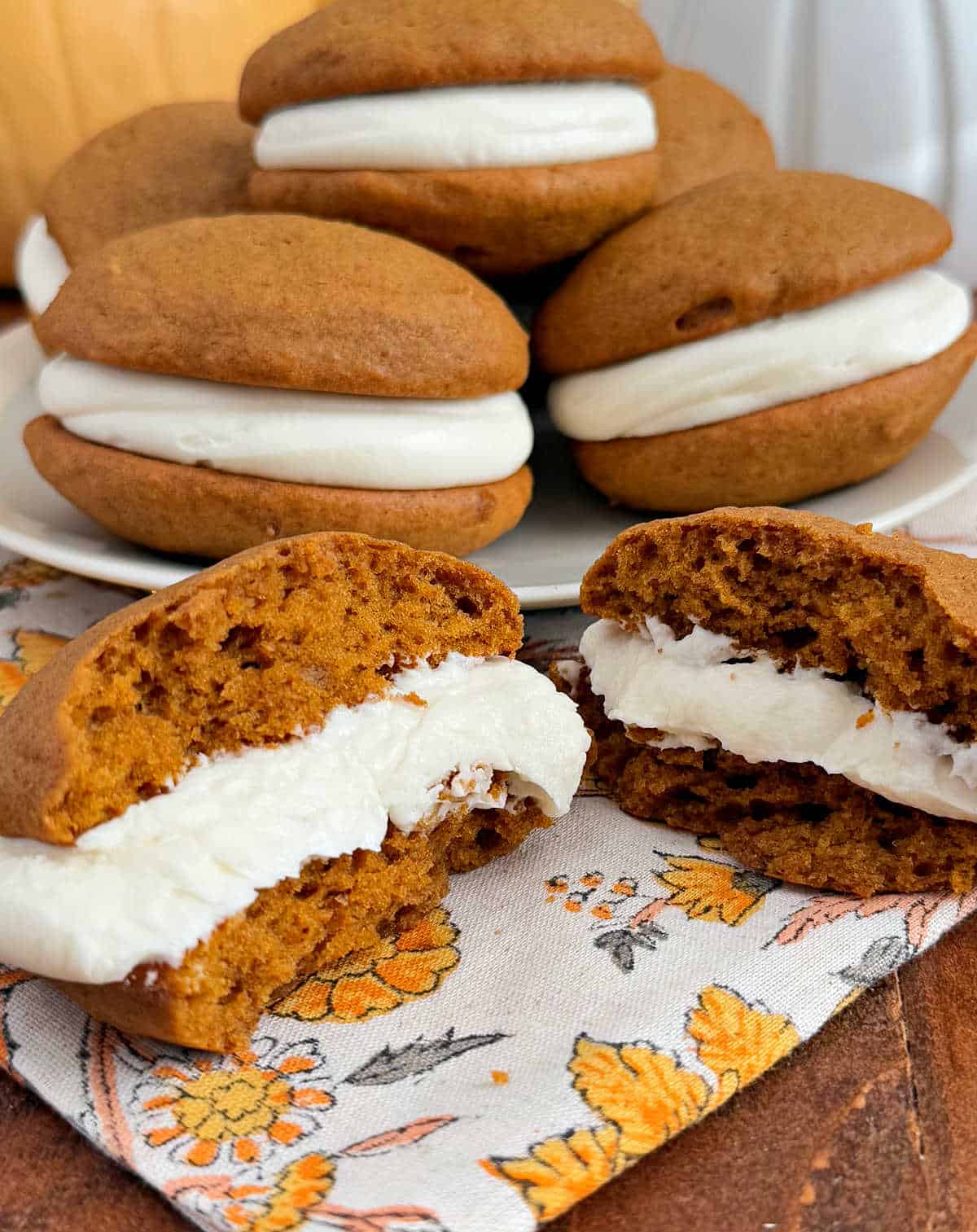 pumpkin whoopie pies on plate and sliced open on table.