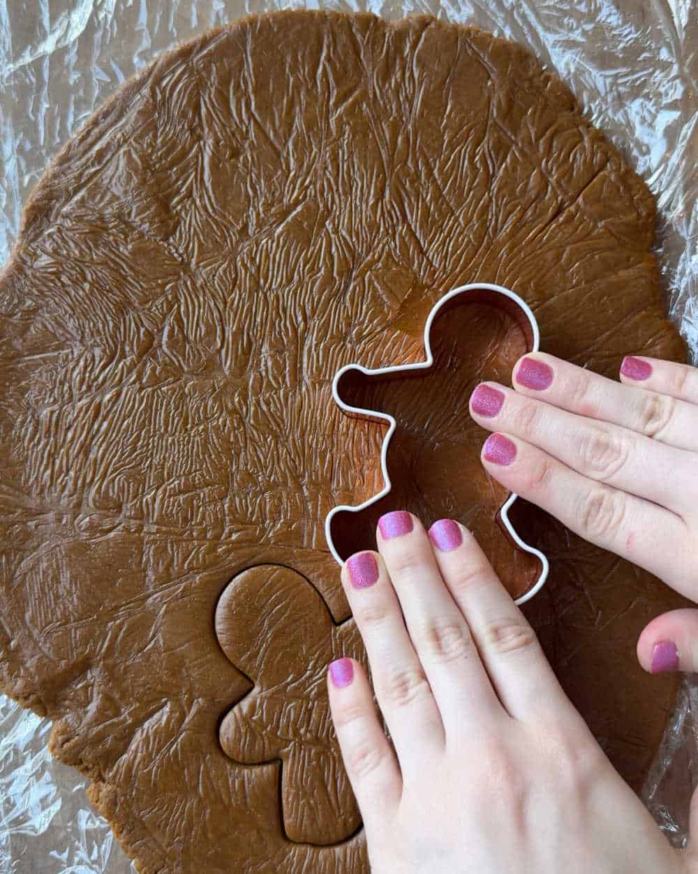 cutting gingerbread men out with cookie cutter.