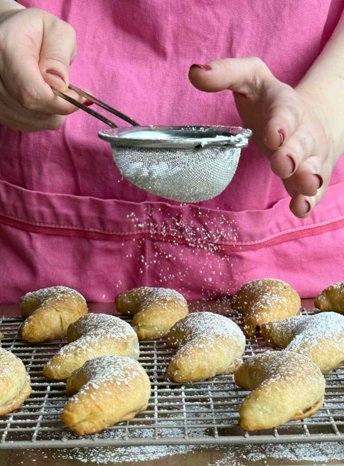 dusting baked nut horn cookies with powdered sugar.