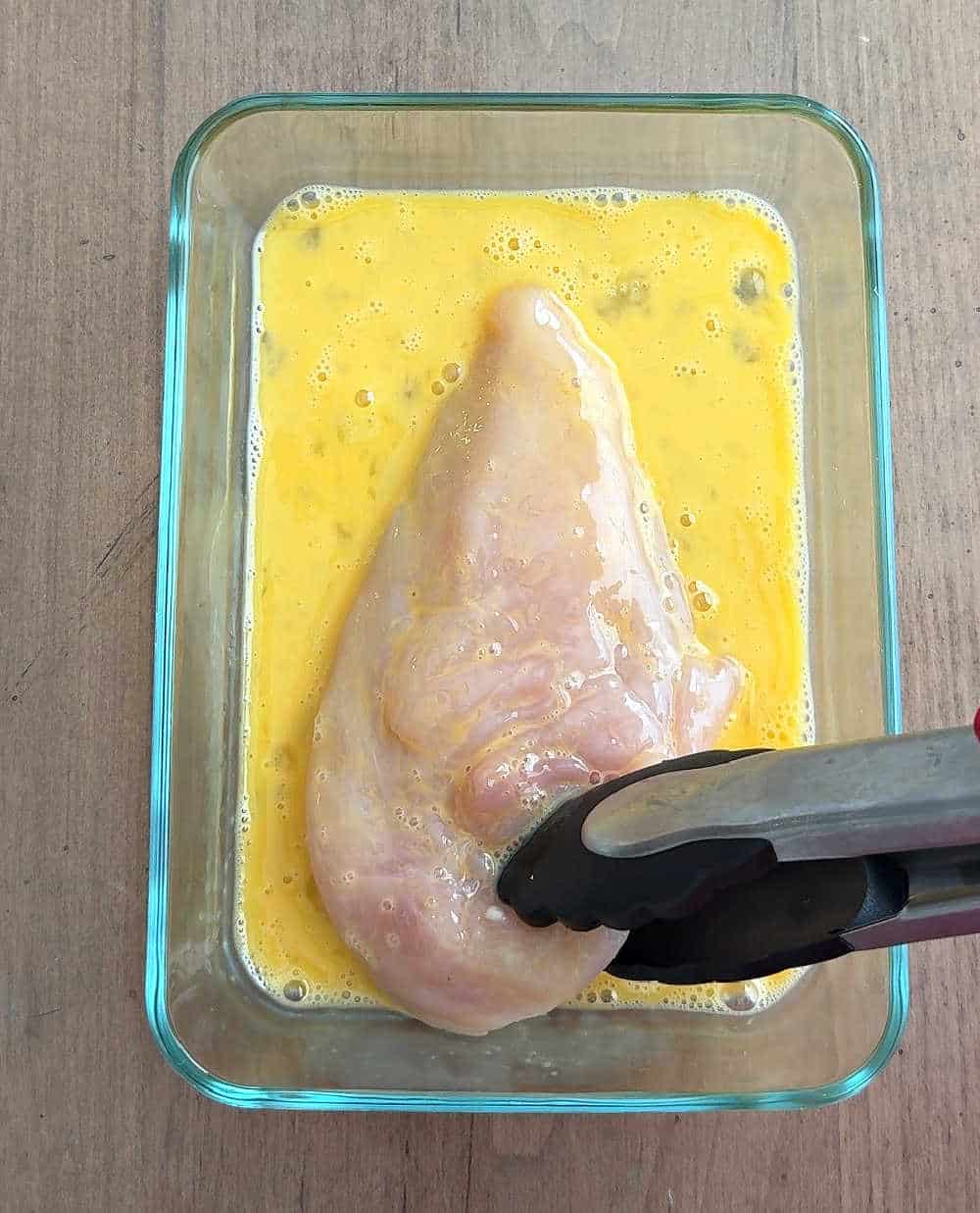 dipping chicken into egg wash.