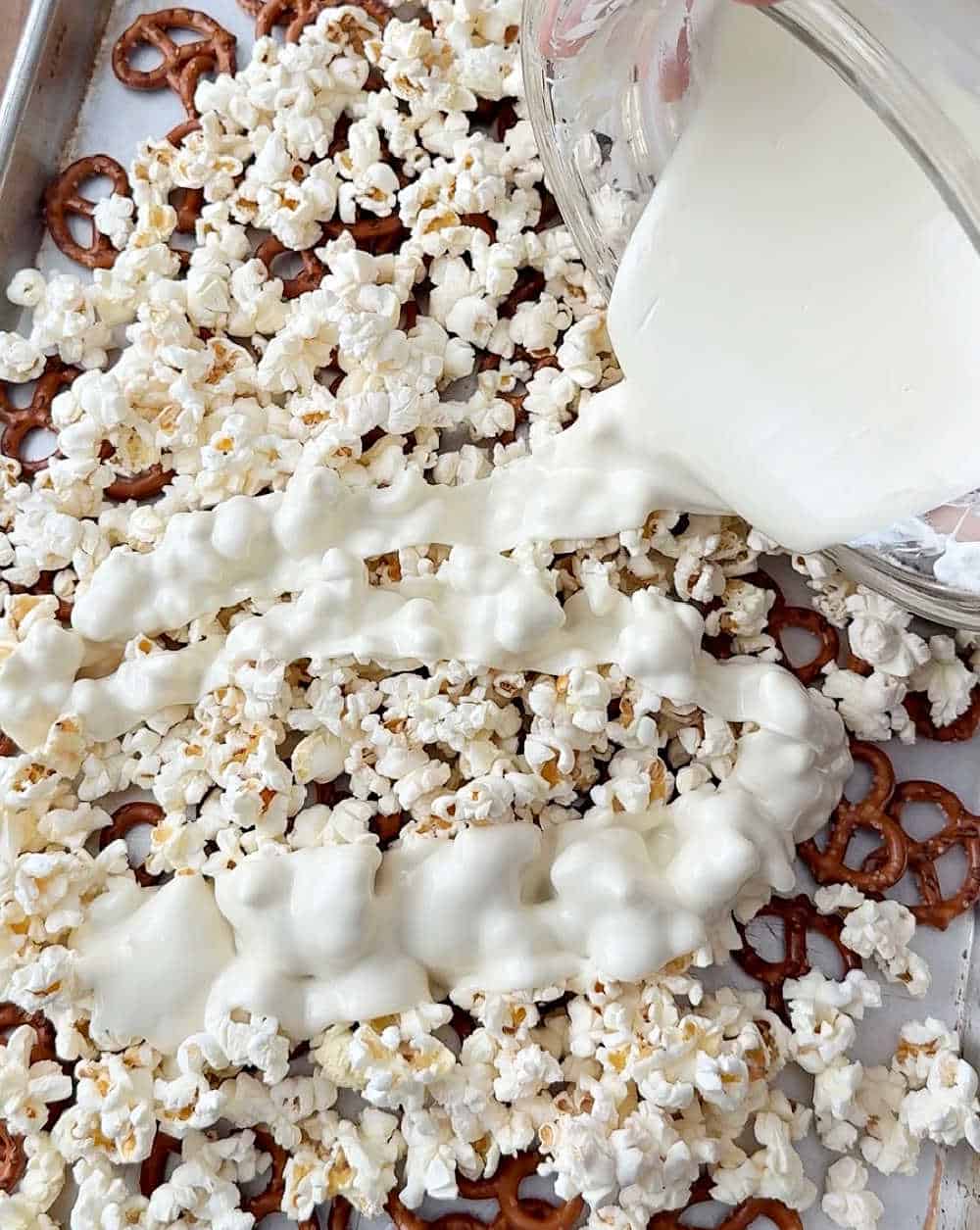 pouring melted white chocolate on popcorn.