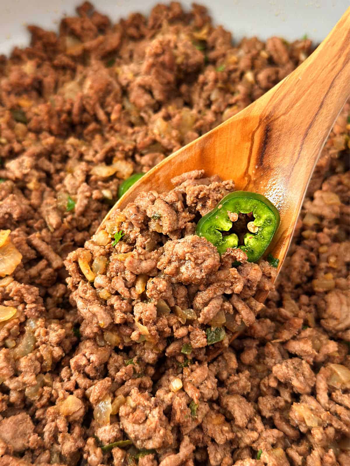 ground beef taco meat with jalapeńo pepper on wooden spoon.