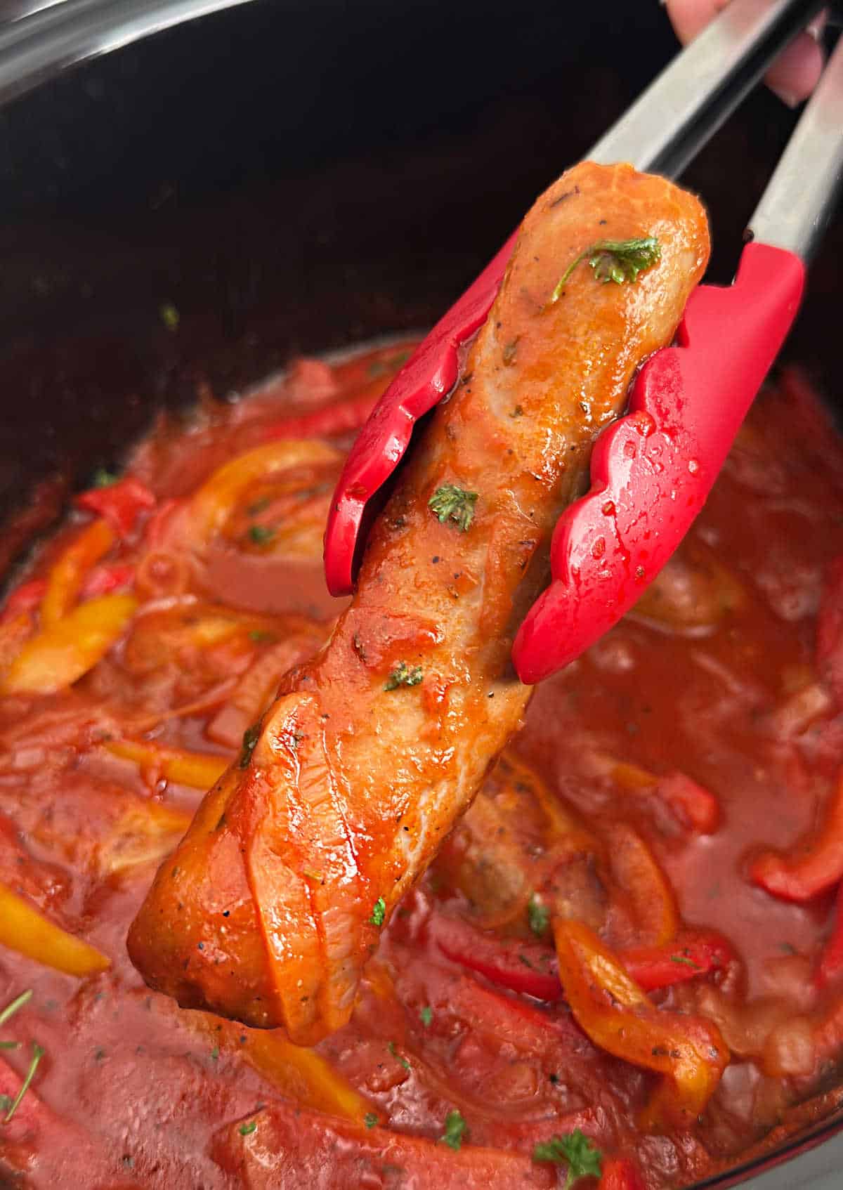 crock pot sausage and peppers in kitchen tongs.