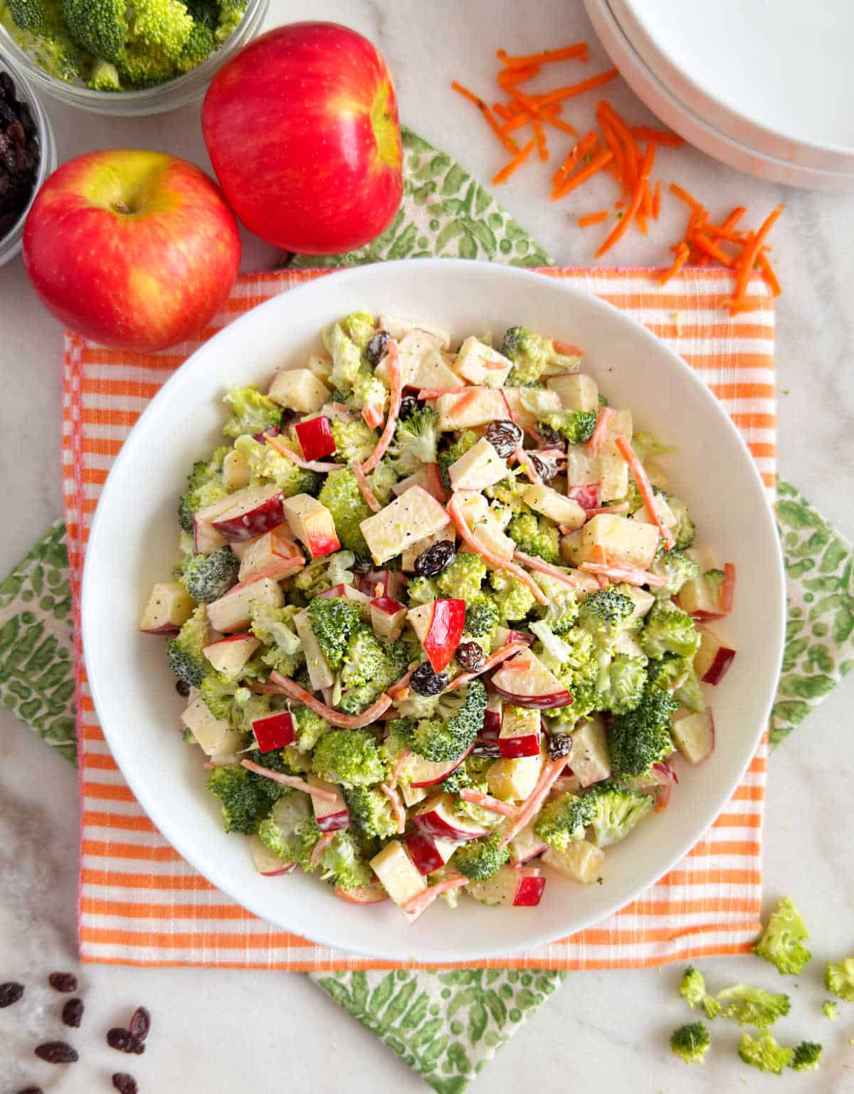 bowl of broccoli apple salad with raisins and carrots on the table.