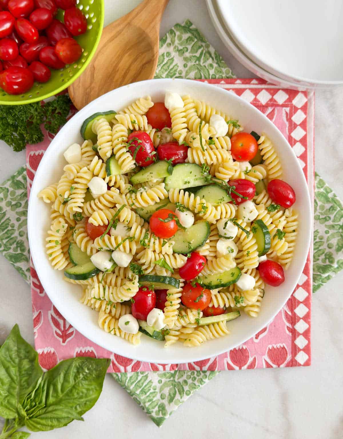 cucumber tomato pasta salad with basil and mozzarella in a white bowl.