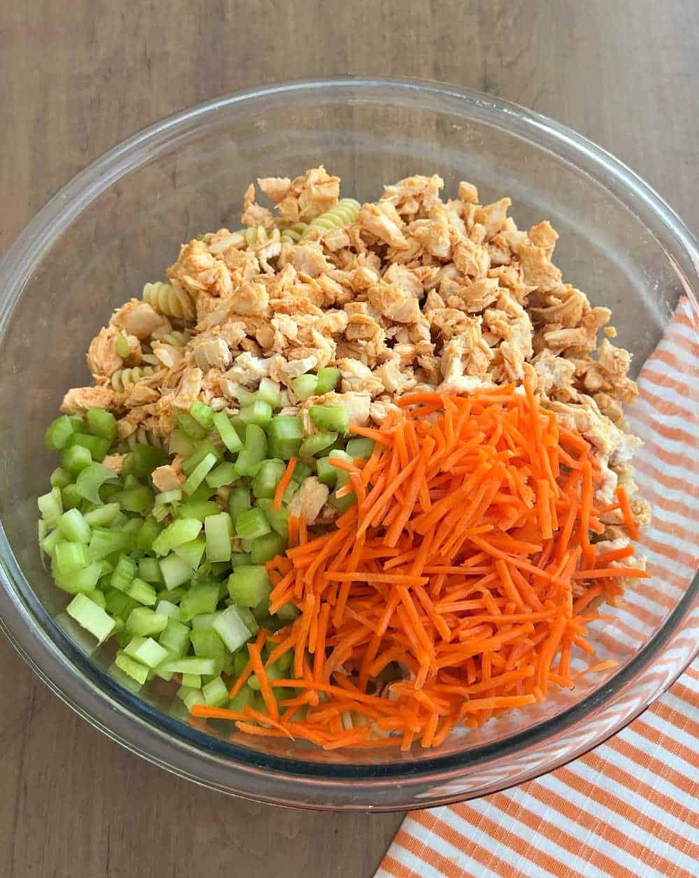 adding carrots, celery and chicken and pasta to bowl.