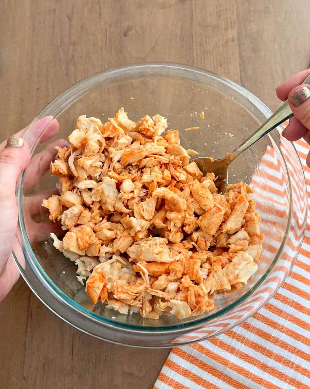 mixing chicken with wing sauce in bowl.