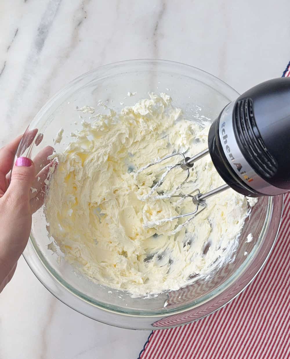 mixing cream cheese with hand mixer in bowl.