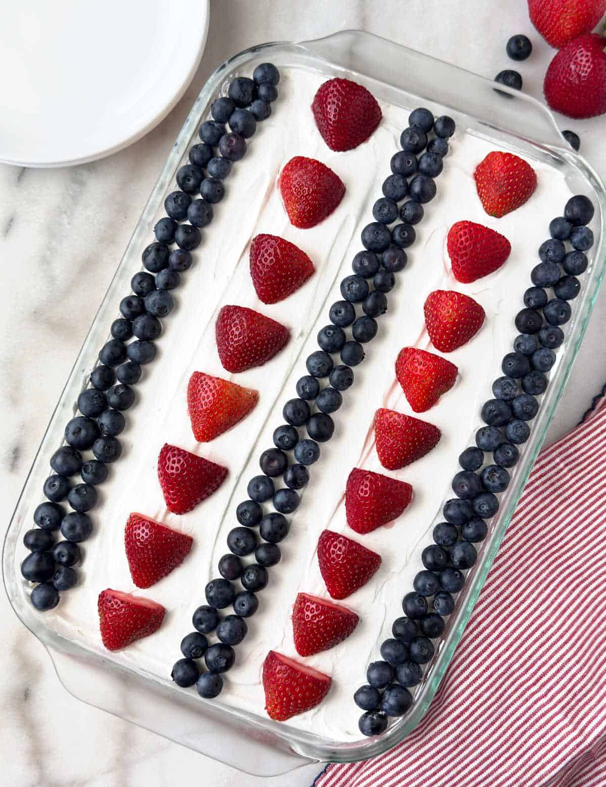 4th of july poke cake in baking dish topped with strawberries and blueberries.