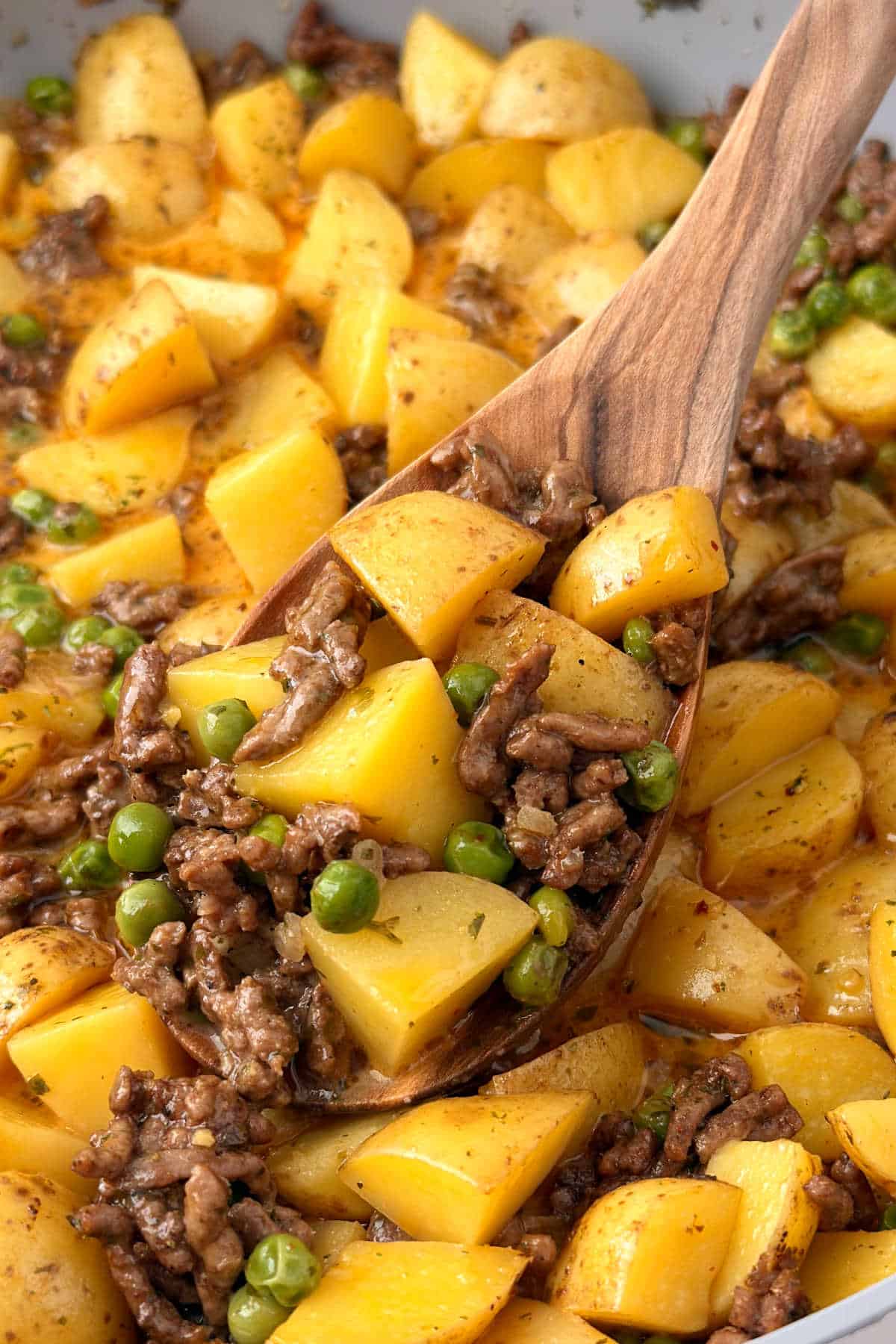skillet ground beef and potatoes with peas on wooden spoon.