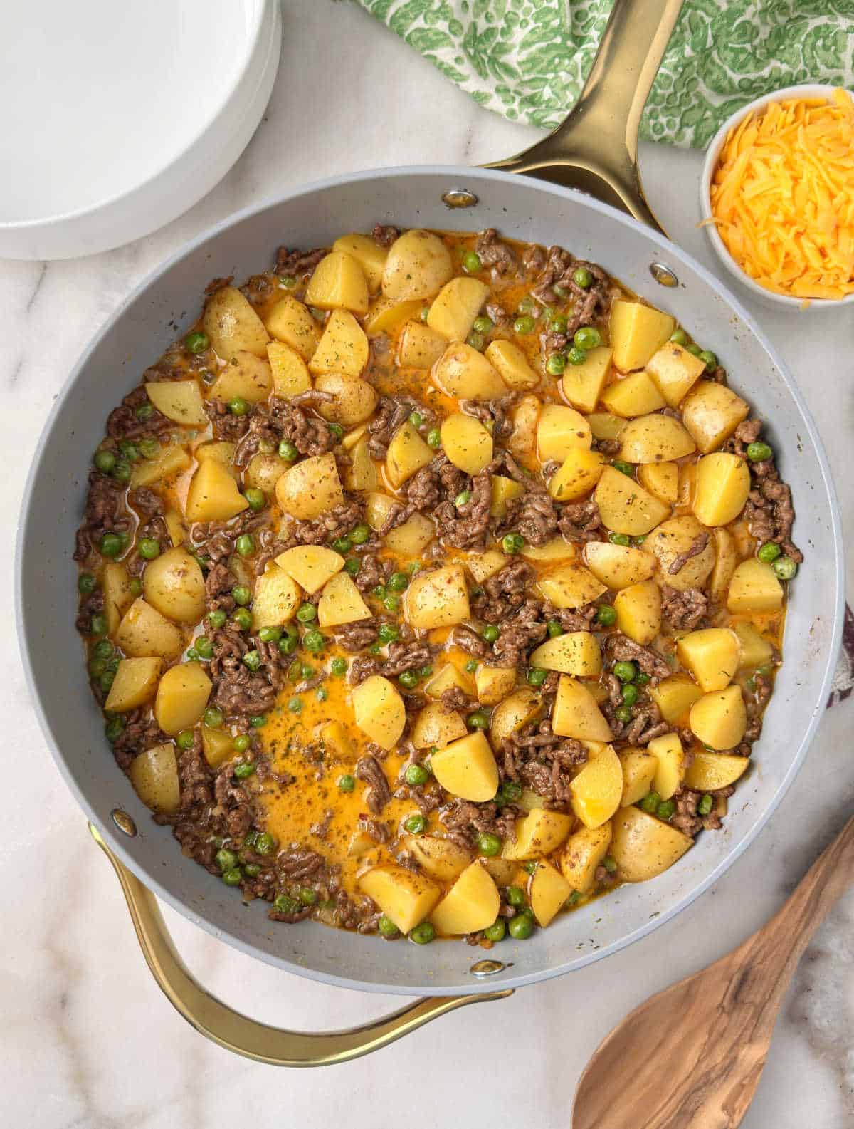 ground beef and potatoes with cheese and peas in skillet.