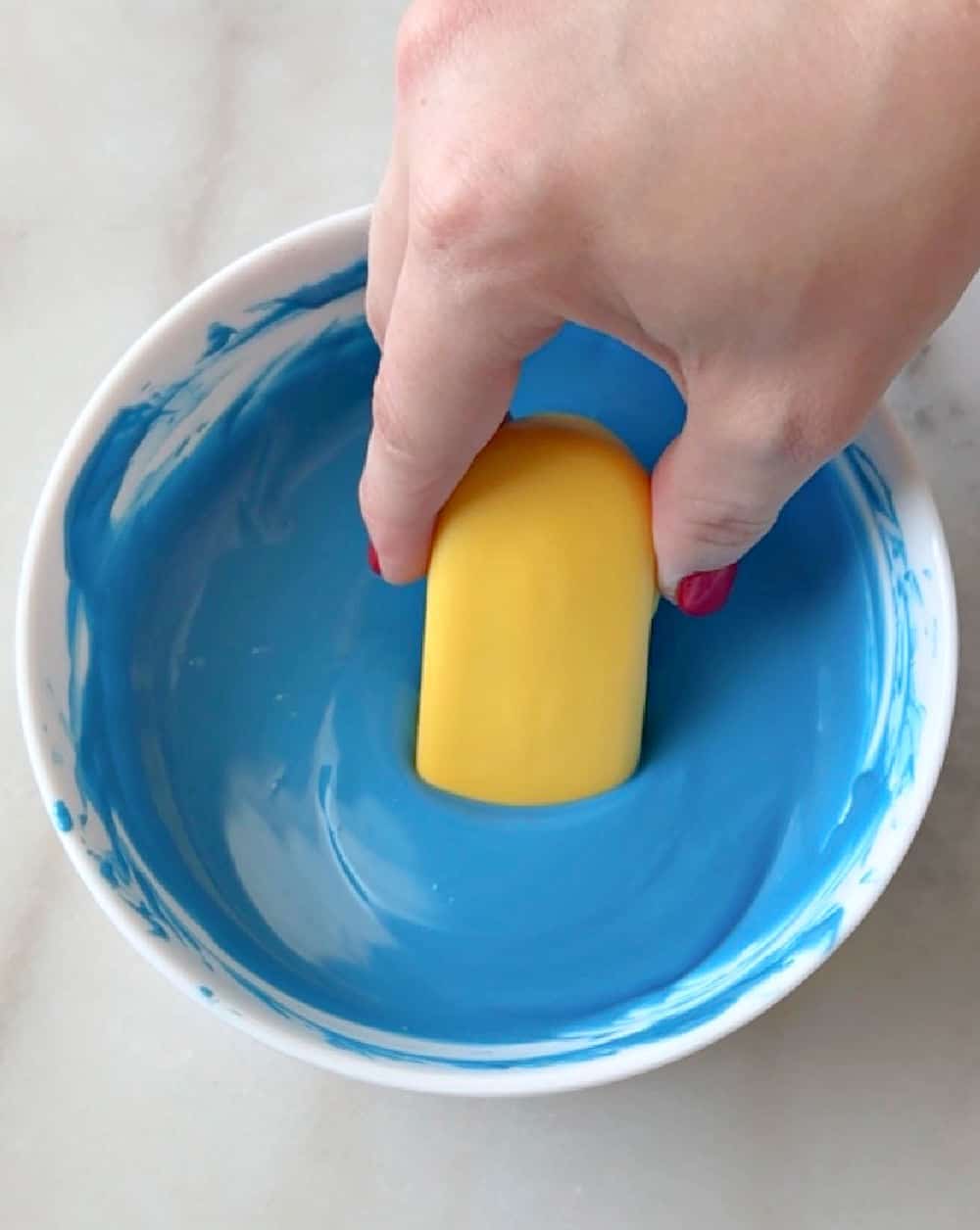 dipping cookie into melted blue coating.