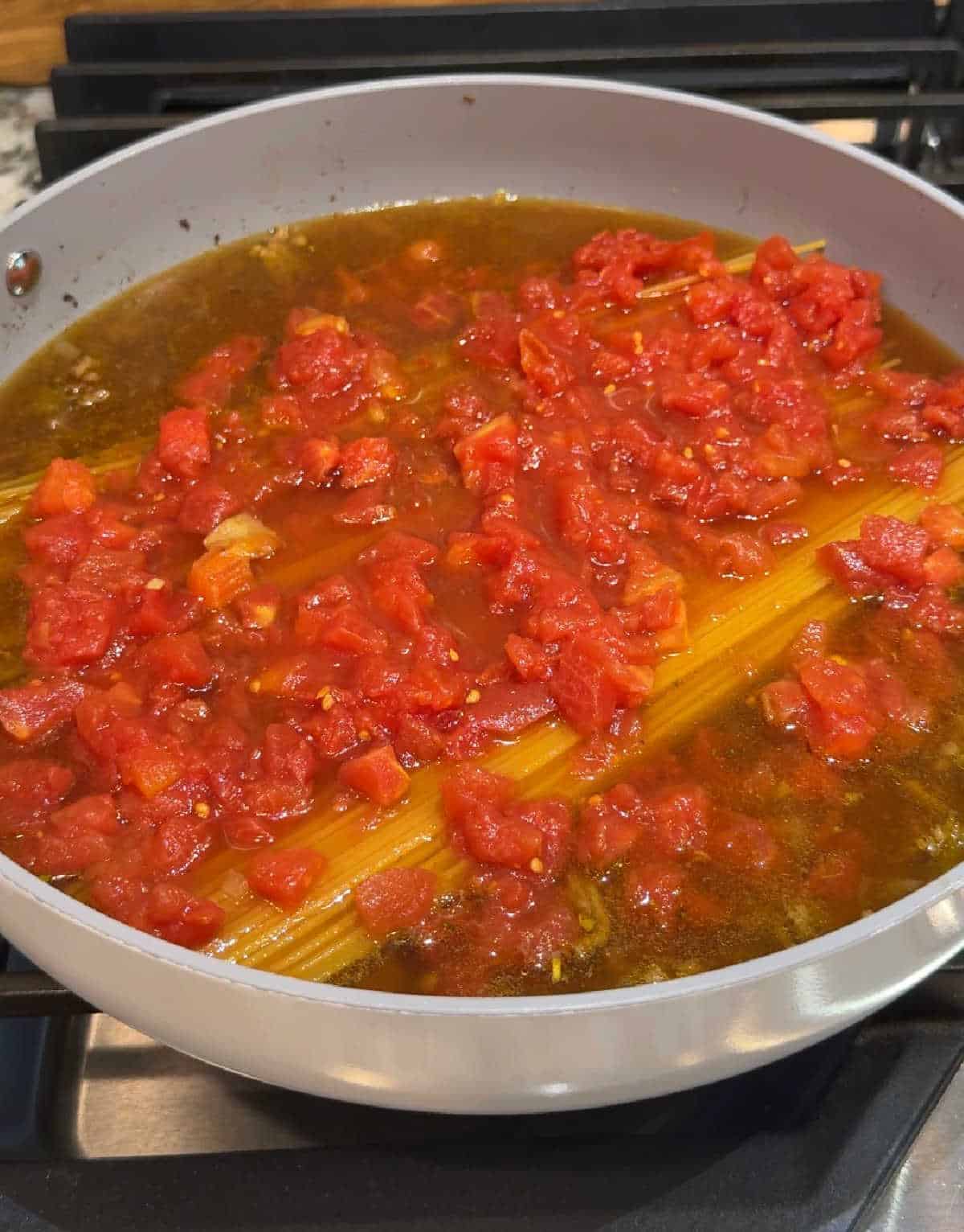 pasta in pan with broth and diced tomatoes.
