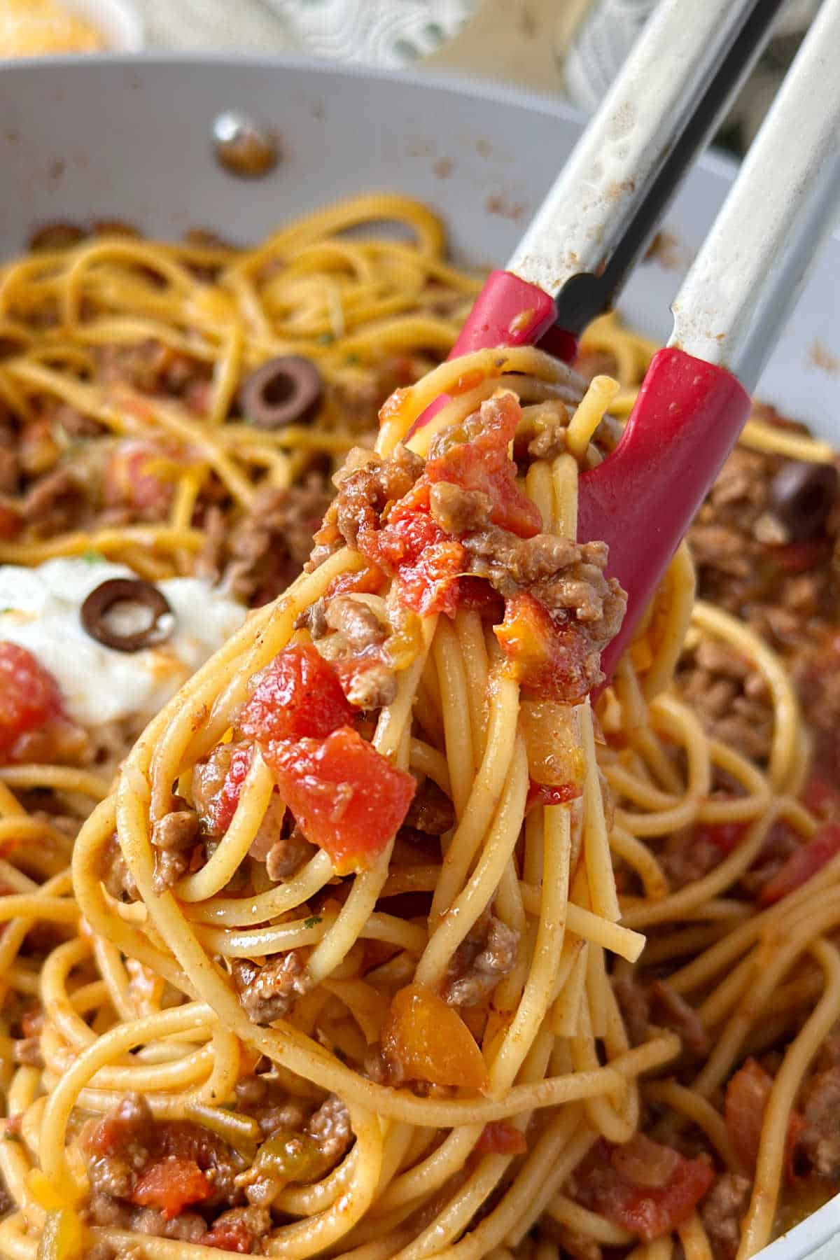 serving taco spaghetti with kitchen tongs.