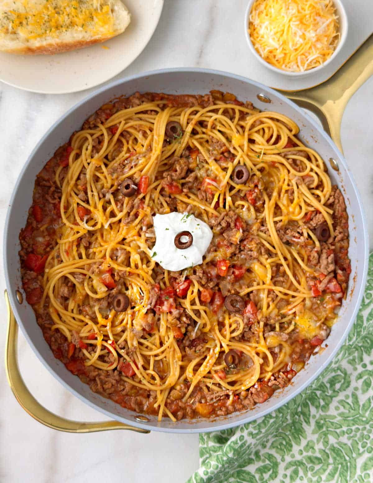 pan of taco spaghetti with tomatoes, olives, sour cream and cheese.