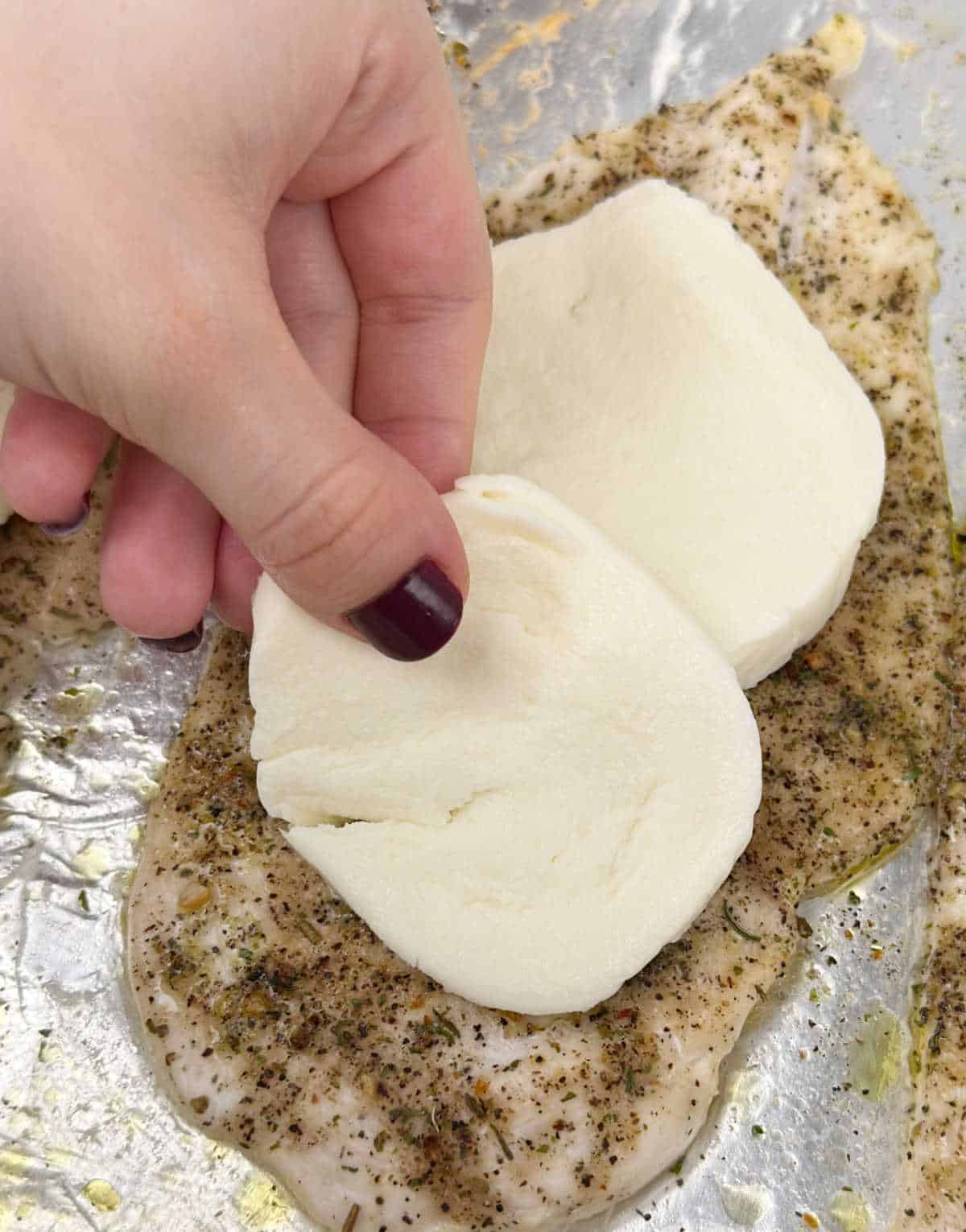 placing mozzarella slices on top of chicken.