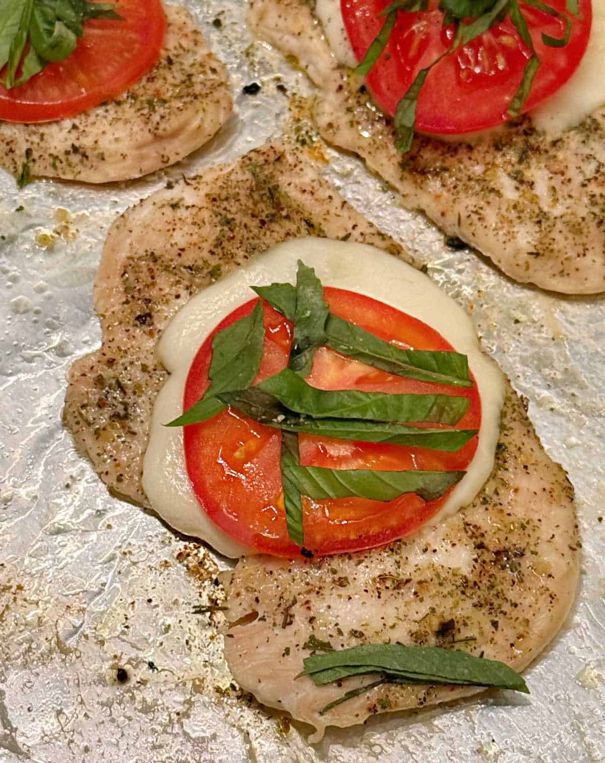 baked chicken with mozzarella, tomato and basil on sheet pan.