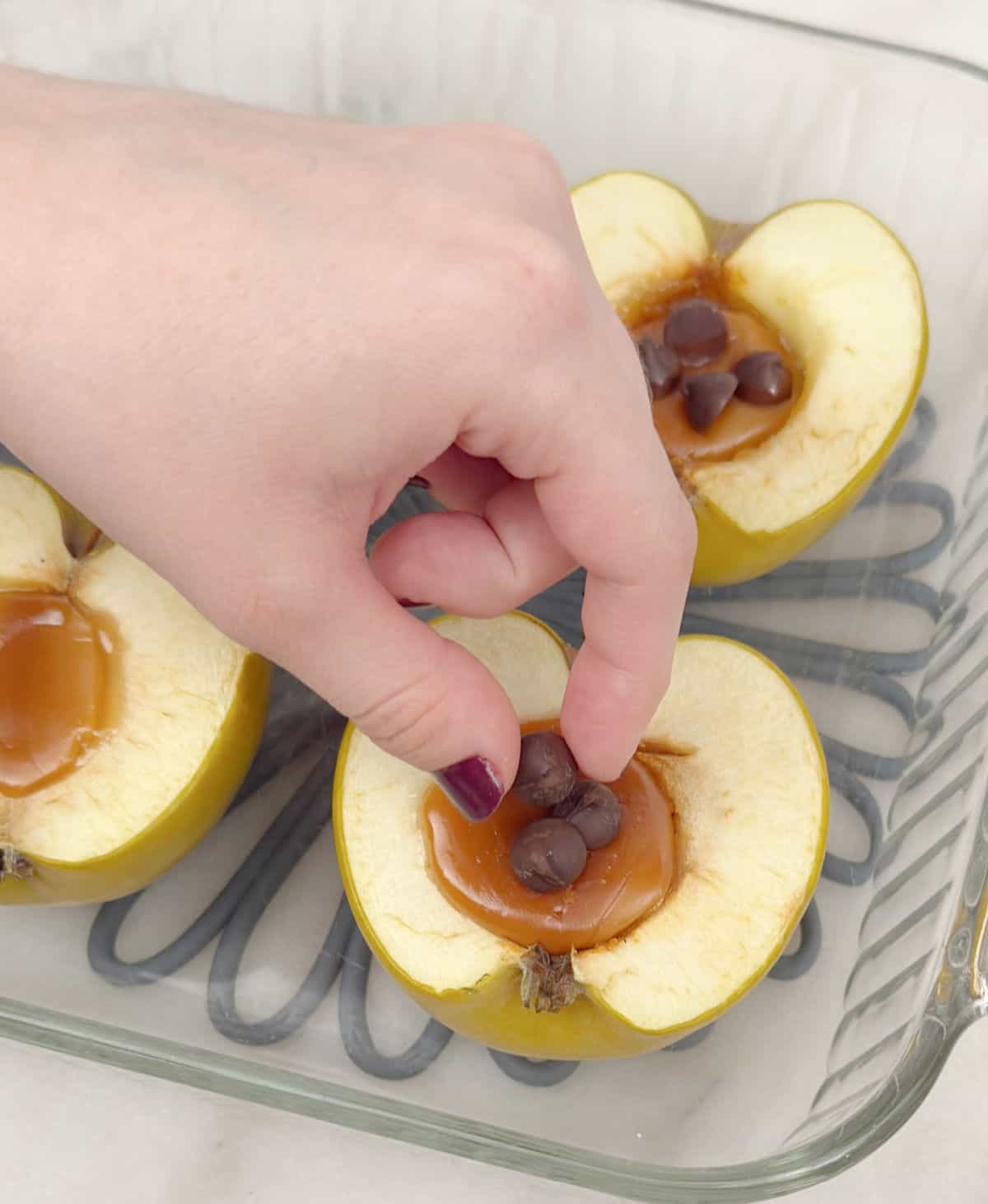 placing chocolate chips on apples stuffed with caramel.