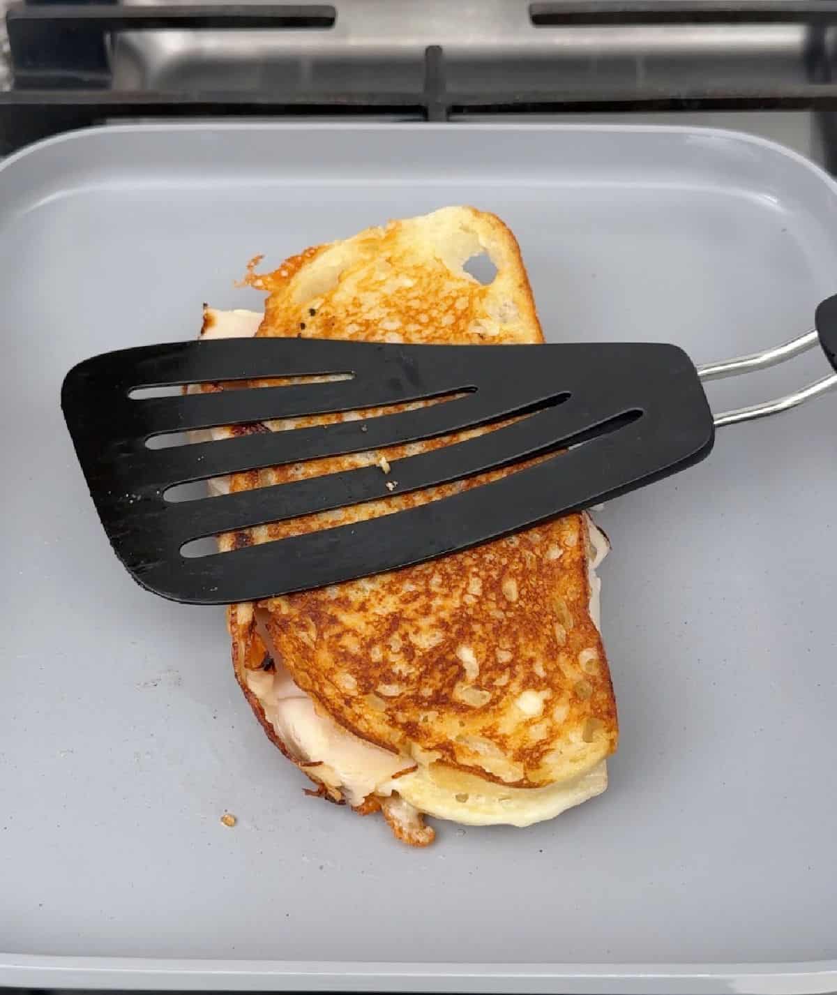 pressing turkey sandwich with spatula on griddle.
