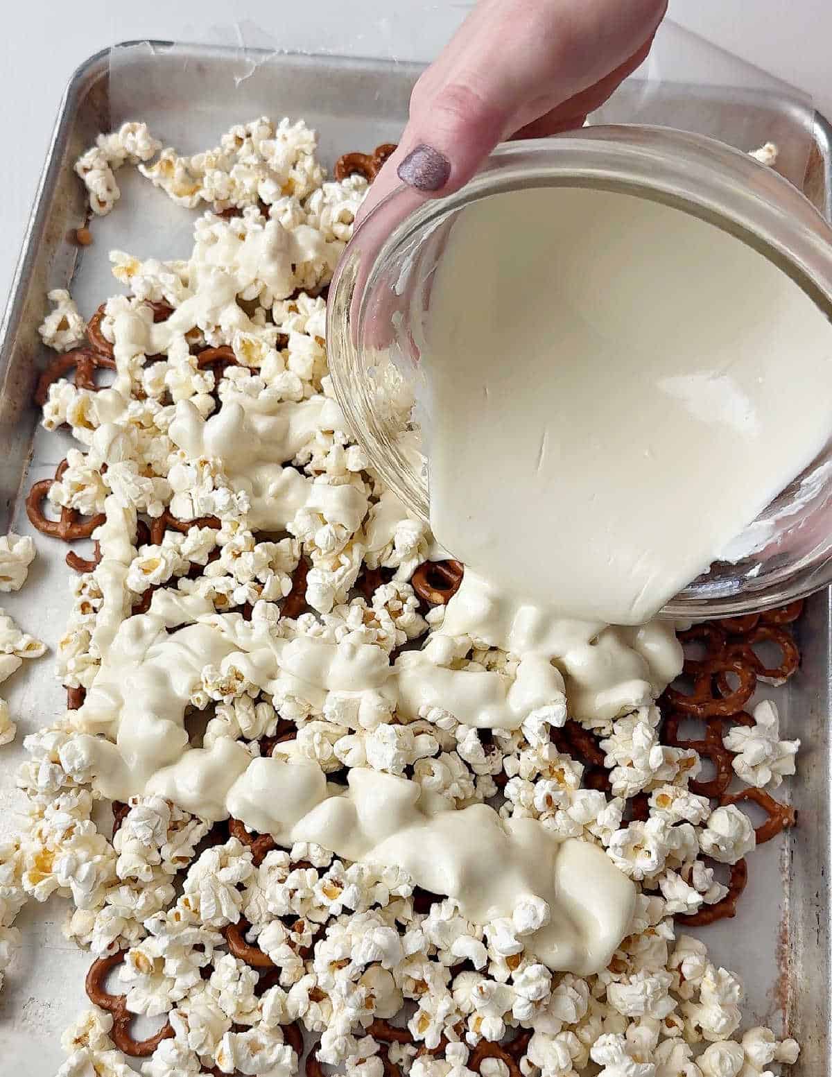 pouring melted white chocolate over popcorn and pretzels.