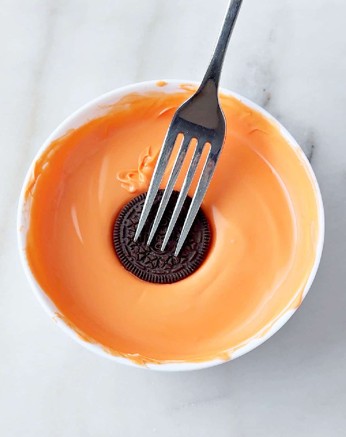 dipping Oreo into orange coating.