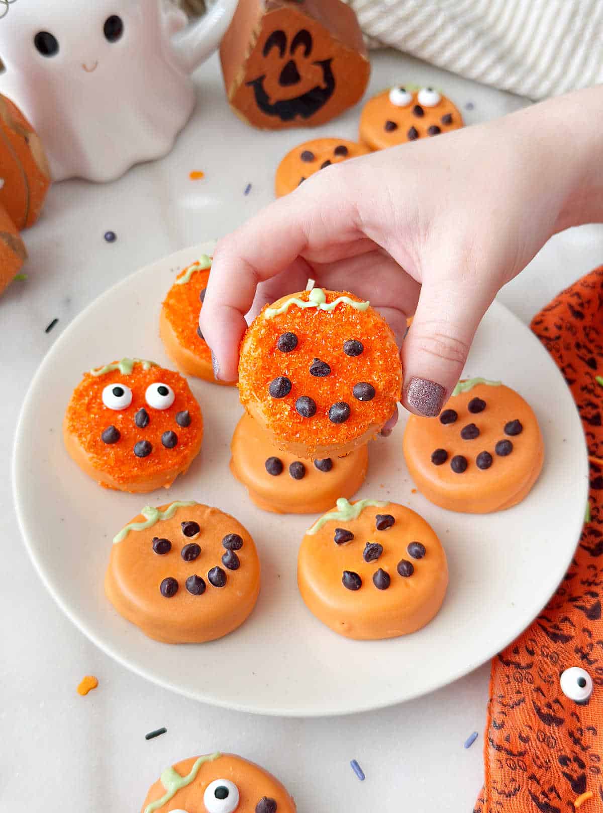 holding a Halloween Oreo pumpkin cookie.