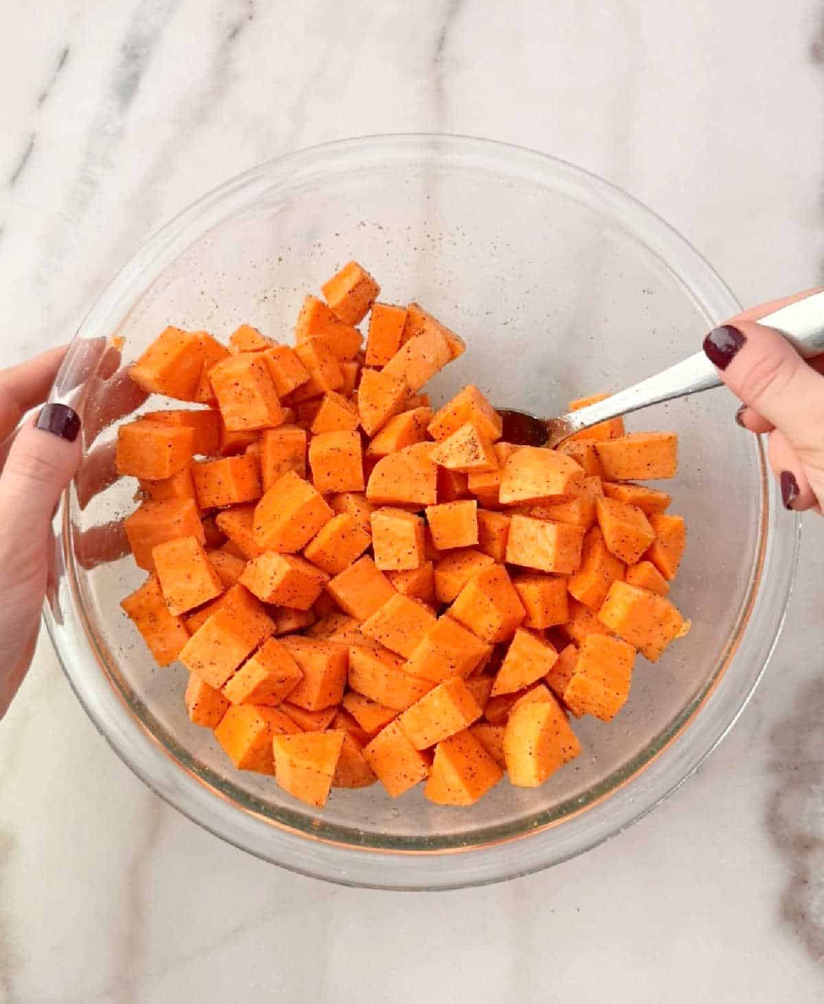 mixing sweet potato cubes with seasonings in bowl.