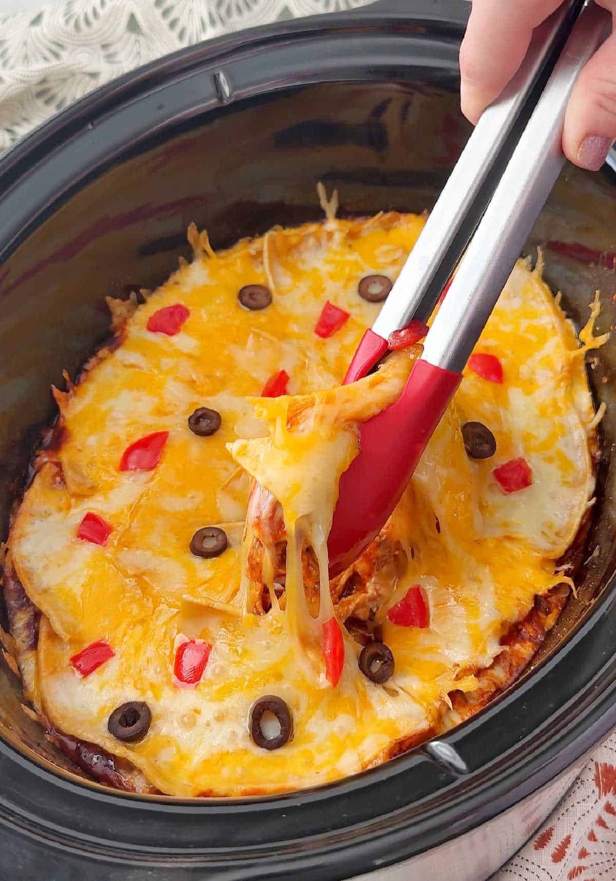 serving cheesy enchilada casserole out of slow cooker with tongs.
