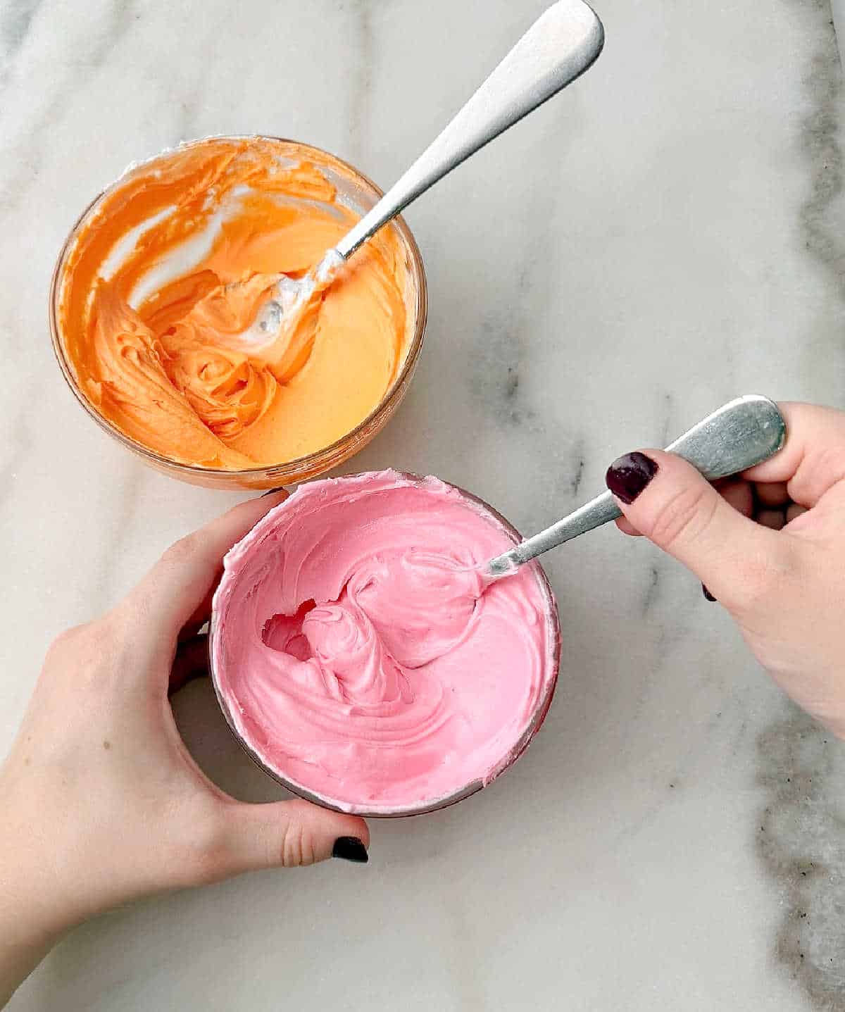 stirring orange and pink icing with spoon.