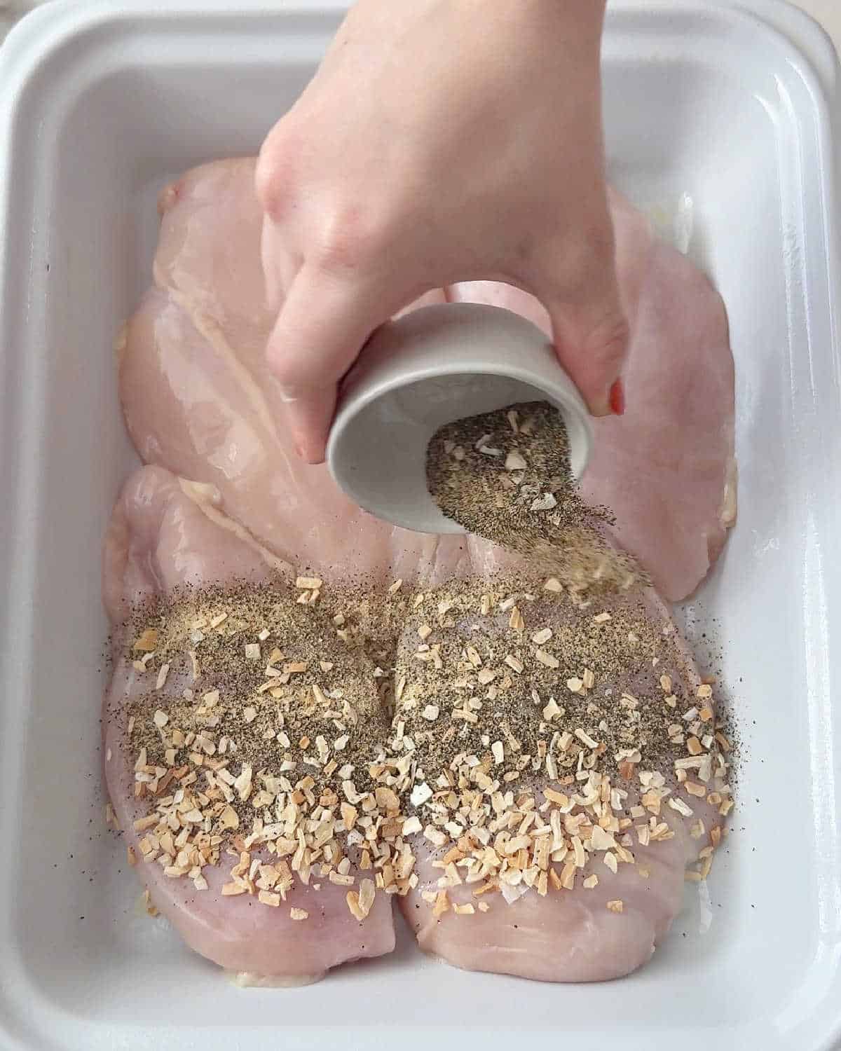 adding seasoning to chicken in baking dish.