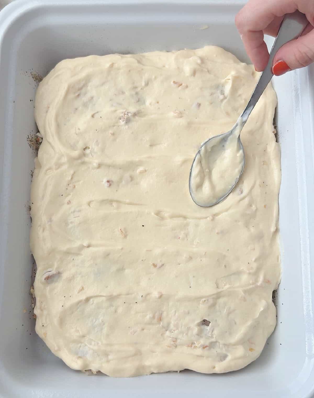 spreading soup mixture on top of chicken with spoon.