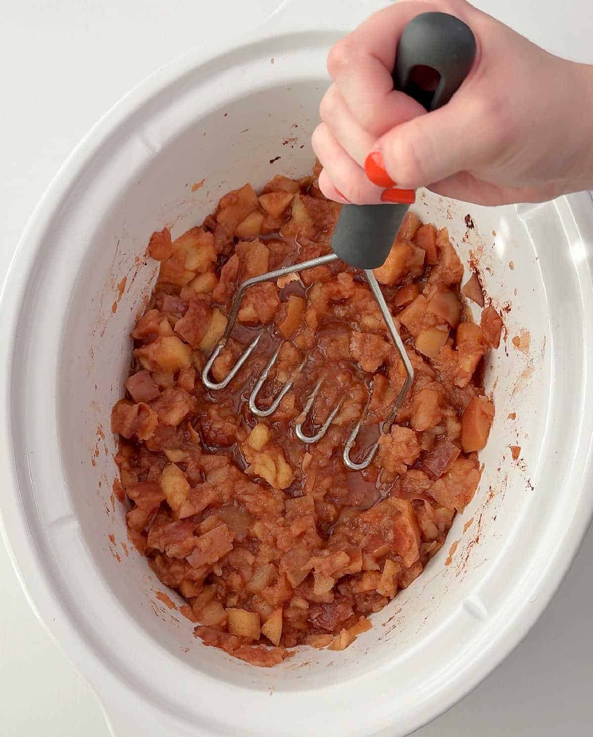 mashing apples in crockpot with potato masher.