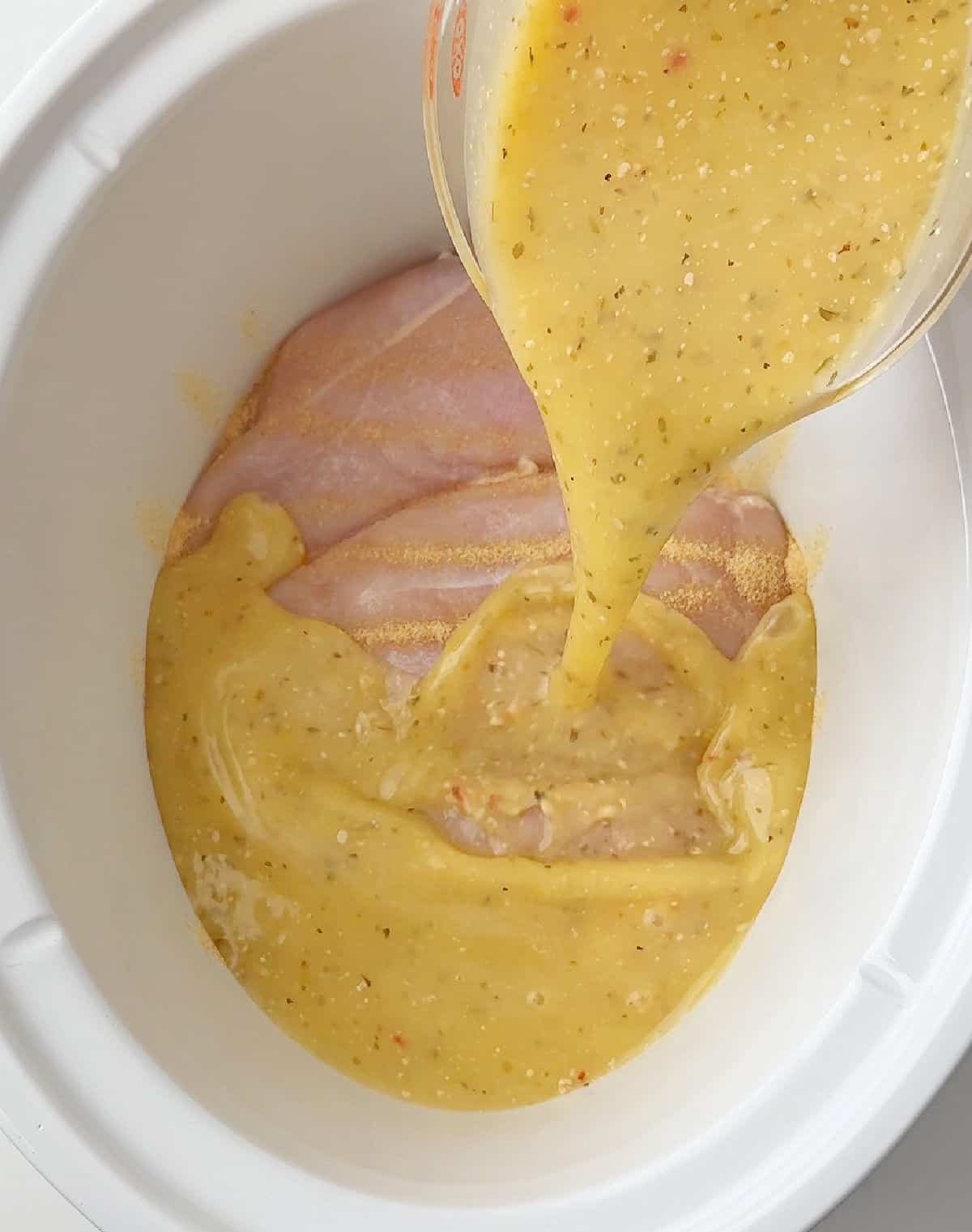 pouring dressing over chicken in slow cooker.