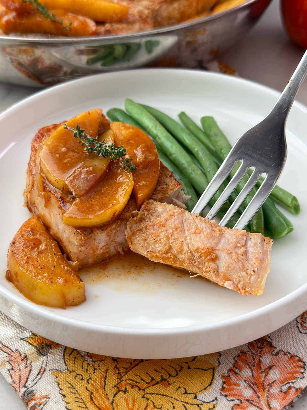 apple cider braised pork chop on a fork with green beans.