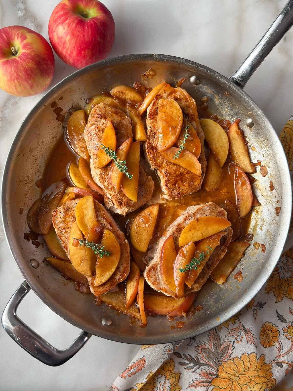 apple cider pork chops with apples and onion in skillet.