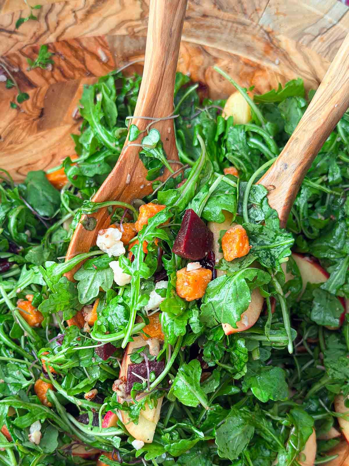 tossing harvest salad with beets and sweet potatoes in bowl.