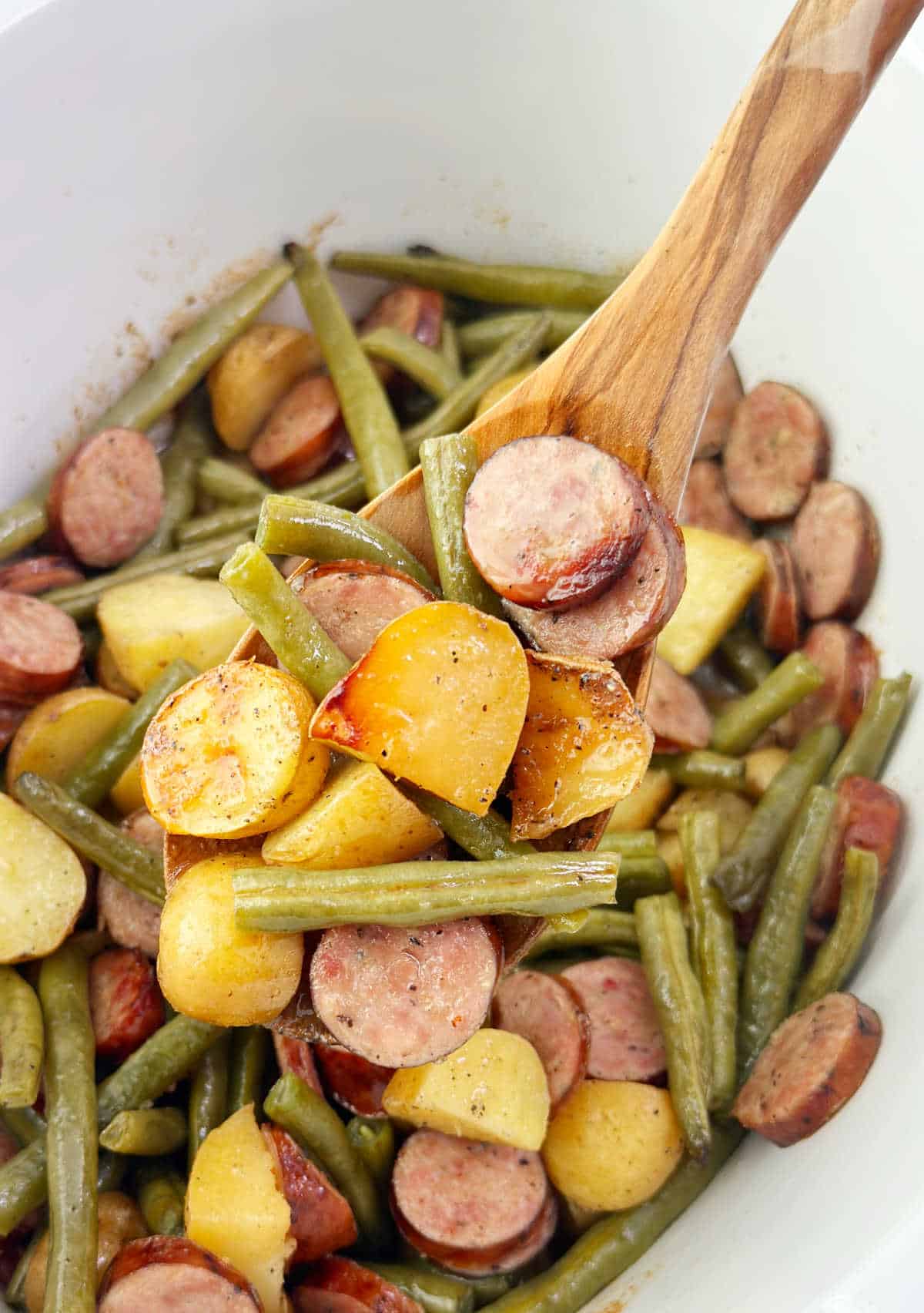 smoked sausage, green beans and potatoes on wooden spoon in slow cooker.