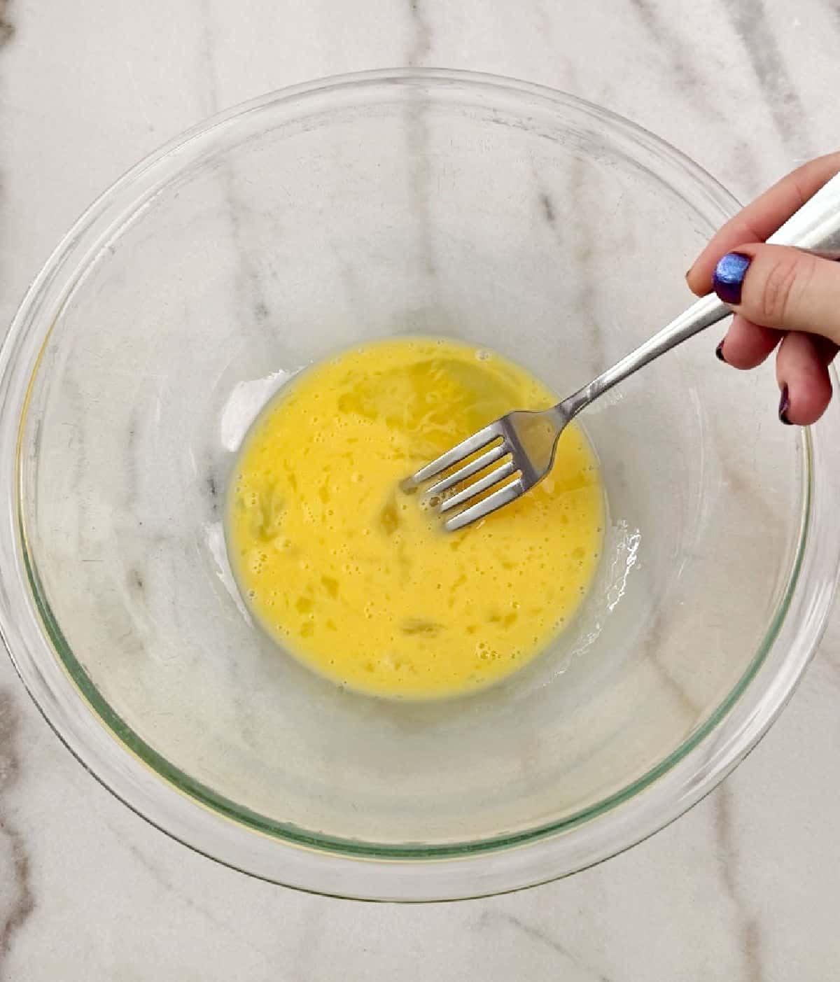 whisking eggs with fork in glass bowl.