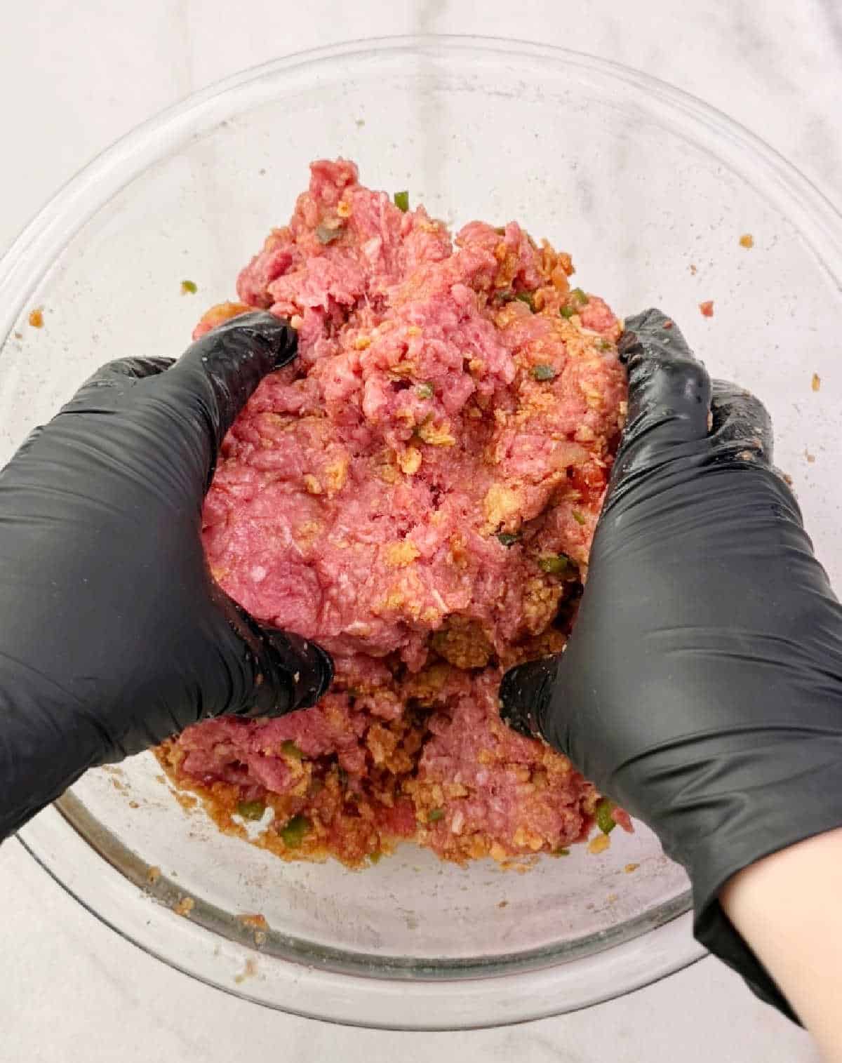 mixing meatloaf mixture in large bowl with gloved hands.