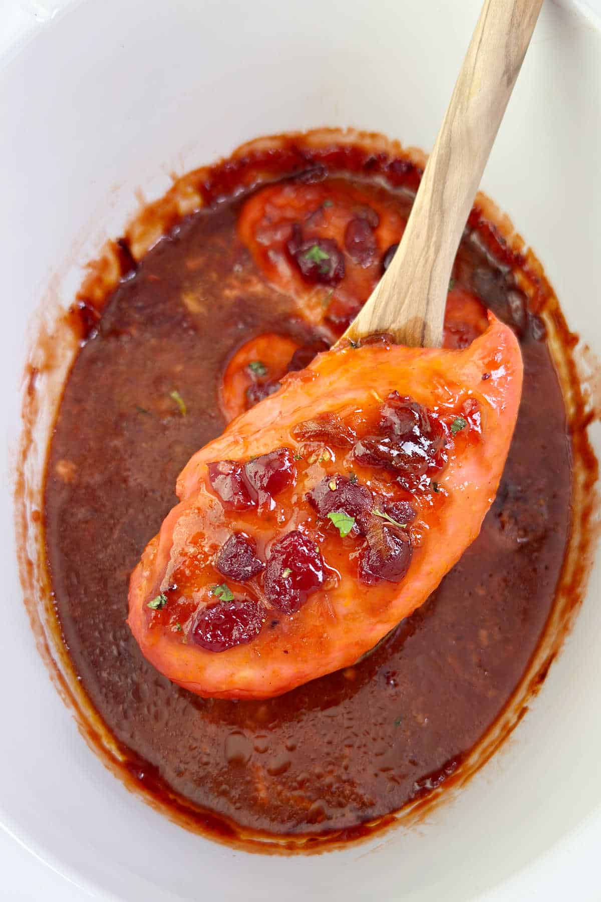 slow cooker cranberry chicken on wooden spoon.